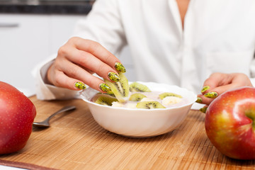 slice of kiwi in a female hand over the plate with yogurt