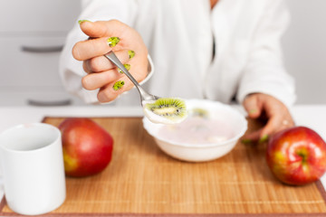 Obraz na płótnie Canvas woman holds out a spoon with yogurt and kiwi