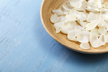 Petals of white roses on blue painted rustic background. Fresh natural flowers in bowl. Dirty grunge wooden board.