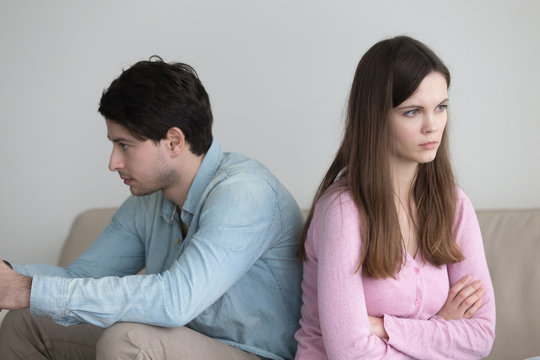 Man and woman sitting serious back to back with arms crossed at home, ignoring and not talking to each other, problems in relationships concept, family conflict, sad after quarrel, having a dispute