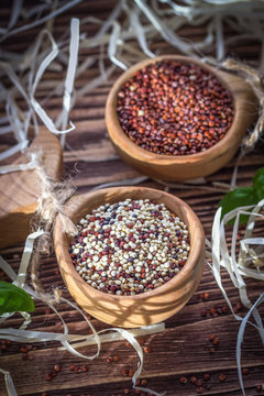Mixed and red raw quinoa seeds in wooden spoons on a brown background
