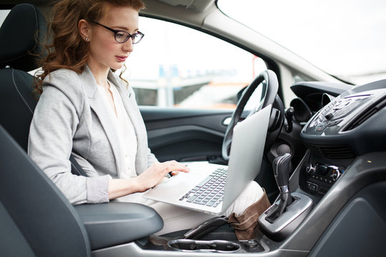 Beautiful female sales manager using laptop and phone in the car.Preparing and looking into contract papers.