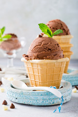 Waffle cups with chocolate ice cream, milk and white chocolate granules in measuring spoons on gray stone background. Healthy summer food concept.