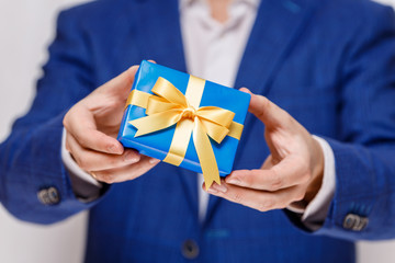 Male hands holding a gift box. Present wrapped with ribbon and bow. Christmas or birthday blue package. Man in suit and white shirt.