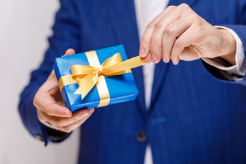 Male hands holding a gift box. Present wrapped with ribbon and bow. Christmas or birthday blue package. Man in suit and white shirt.