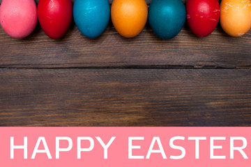 Closed, colored in different bright colors chicken eggs for the holiday Easter on natural wooden background with white text Happy Easter on pink rectangle