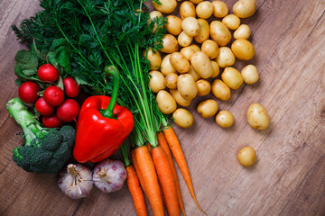 Potatoes with carrot, garlic and pepper. Red radish, brocoli and raw new potato. Fresh natural vegetables. Organic bio food. On wooden table.