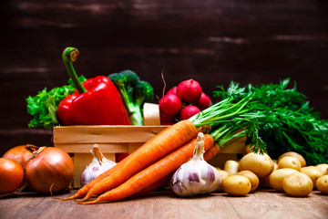 Vegetables. Potatoes, carrot and red pepper. Lettuce salad, garlic and brocoli. Onion and radish. Wooden basket on rustic table.