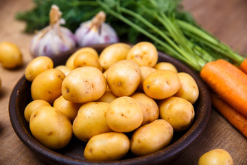 Potatoes in plate. Carrot, garlic and raw new potato. Fresh natural vegetables. Organic bio food on rustic wooden table.