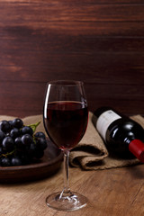 Red wine. Bottle with wineglass. Dark grapes branch on plate. On rustic wooden background.