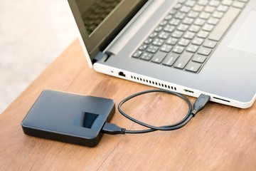 Technology concept : External hard disk and laptop computer with warm light effect. External hard drive connected to laptop on wooden table with copy space.