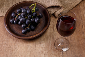 Red wine. Wineglass with dark grapes branch on plate. On rustic wooden background.