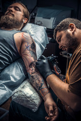Fototapeta premium Tattoo master showing process of making a tattoo in tattoo parlor