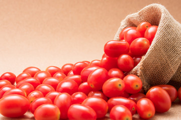 Red cherry tomatoes in burlap sack on brown table background