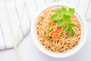 Instant noodles in paper bowl on white wooden background.
