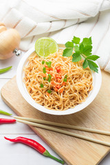 Instant noodles in paper bowl on white wooden background.