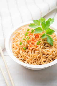 Instant noodles in paper bowl on white wooden background.