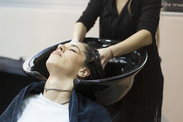 Fototapeta premium Beautiful young woman with hairdresser washing head at hair salon