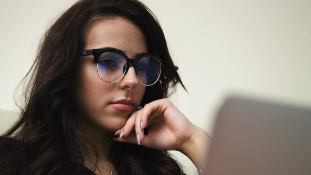 Close up portrait of young attractive woman in glasses looking at the laptop screen