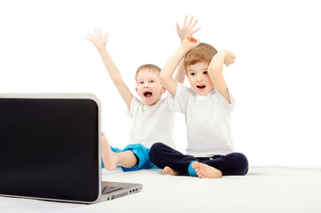 Two joyful children, sitting in front of a laptop screen, isolated on a white background
