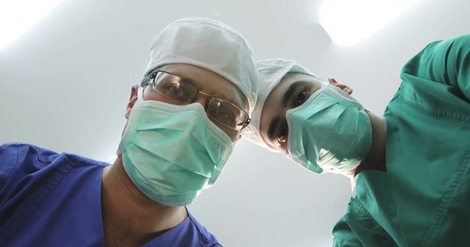 Doctors in masks and medical uniforms looks down at patient.