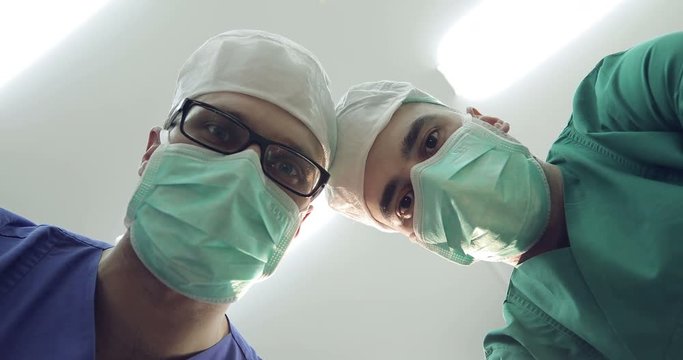 Doctors in masks and medical uniforms looks down at patient.
