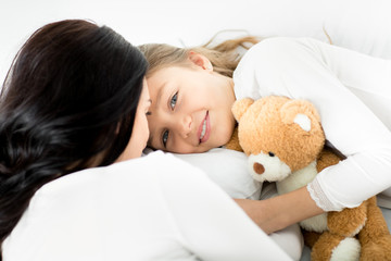 Adorable daughter with teddy bear and mother relaxing on bed at home