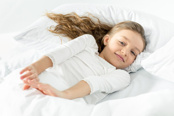 Adorable little girl in white sleepwear awakening in bed at home