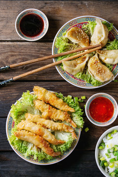Fried tempura shrimps and gyozas potstickers on lettuce salad with sauces and rice. Served in traditional china plate with chopsticks over old wooden background. Top view. Asian dinner