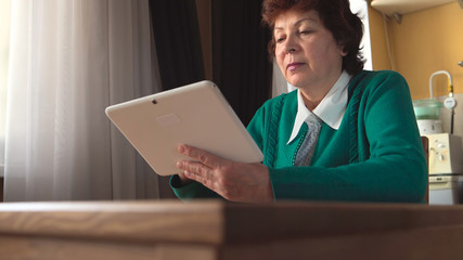 Aged woman uses a white tablet PC at home - Side view