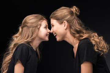 Side view of beautiful happy mother and daughter smiling together on black