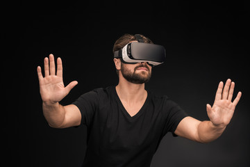Young bearded man in black t-shirt wearing virtual reality headset on black