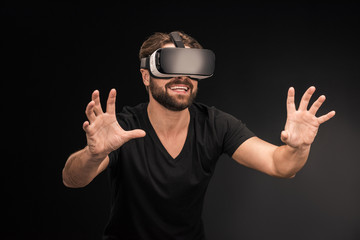 Young bearded man in black t-shirt wearing virtual reality headset on black