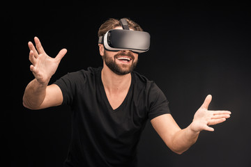 Naklejka premium Young bearded man in black t-shirt wearing virtual reality headset on black