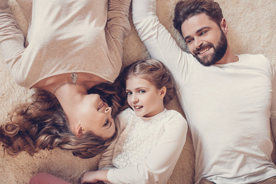 Top view of happy family with one child lying together on carpet