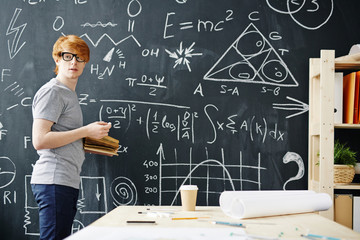 Portrait of young red haired student working at big blackboard writing science formulas in college...