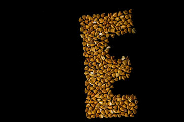 Letter E written with buckwheat on a black background