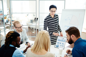 Obraz premium Analyzing statistical data at business meeting: multiethnic group of financial managers gathered together and discussing working results