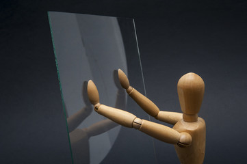 Conceptual image using a wooden dummy as subject and representing a person having the palms of his hands against a glass surface.