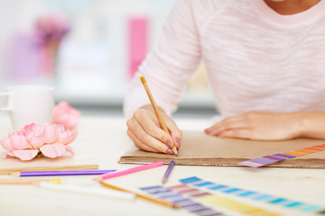 Naklejka premium Close-up shot of female hands taking notes, color swatches, pencils and flowers lying on white desk