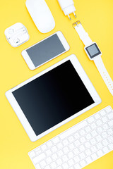 Flat lay of office supplies, keyboard, digital tablet, smartwatch and smartphone on yellow