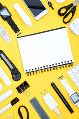 Flat lay of office supplies, digital devices and notepad on yellow