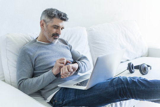 Mature man at home using laptop and checking the time