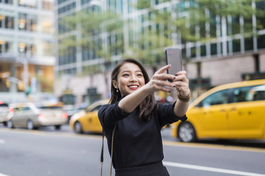 USA, New York City, Manhattan, portrait of smiling young woman taking selfie with smartphone