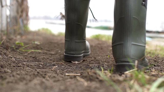 Gardener wearing rubber boots raking soil on sunny day. Slow motion