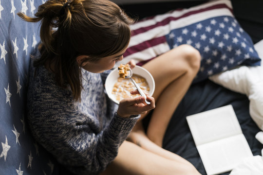 Top view of young woman eating cereals and reading book