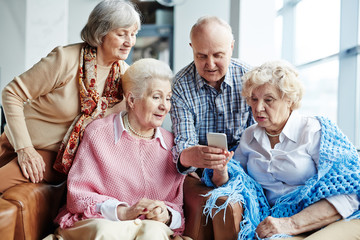 Tech-savvy senior man teaching his female friends how to write SMS message while they gathered together in cafe