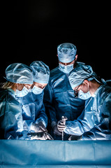 The doctor makes sternotomy during a thoracic operation. Doctors are dressed in
one-off blue surgical suits, on their faces they have medical masks, and on their heads surgical caps. - 142468806