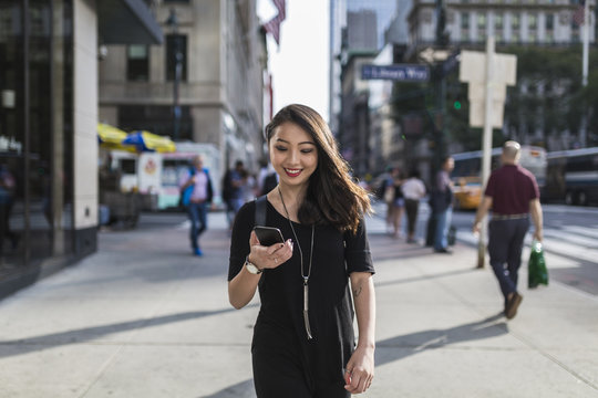 USA, New York City, Manhattan, portrait of smiling young woman dressed in black looking at cell phone