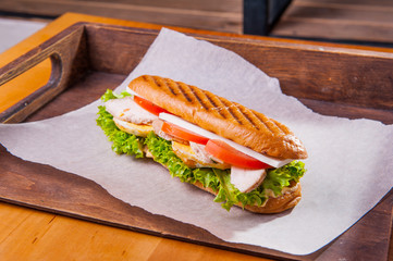 Ciabatta Chiken Sandwich with lettuce, slices of fresh tomatos, scrambled eggs and mozzarella cheese on the white craft paper. Take out food concept. Selective focus